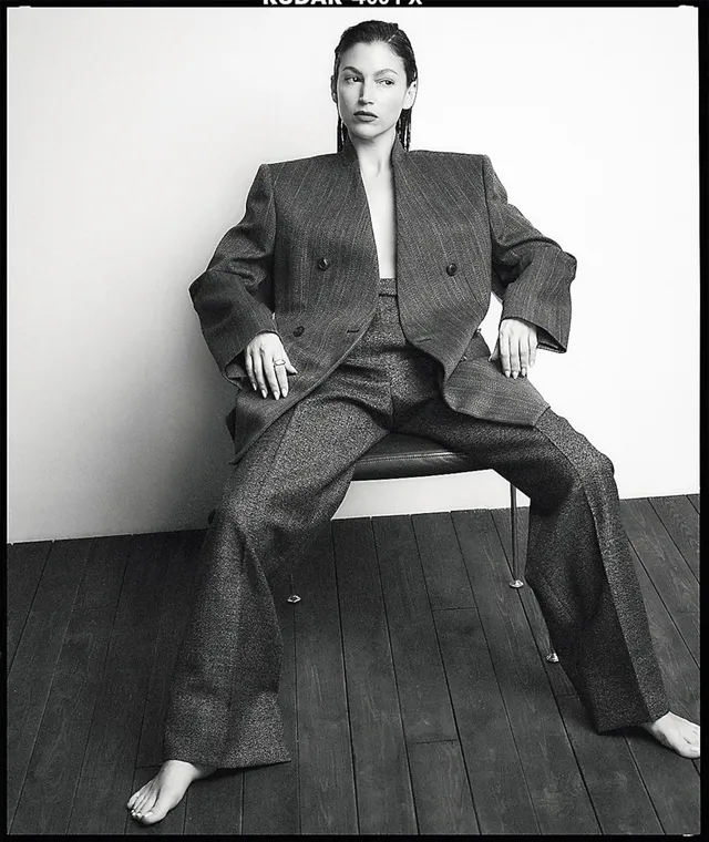 Úrsula Corberó sitting barefoot in an oversized suit for a monochrome portrait.