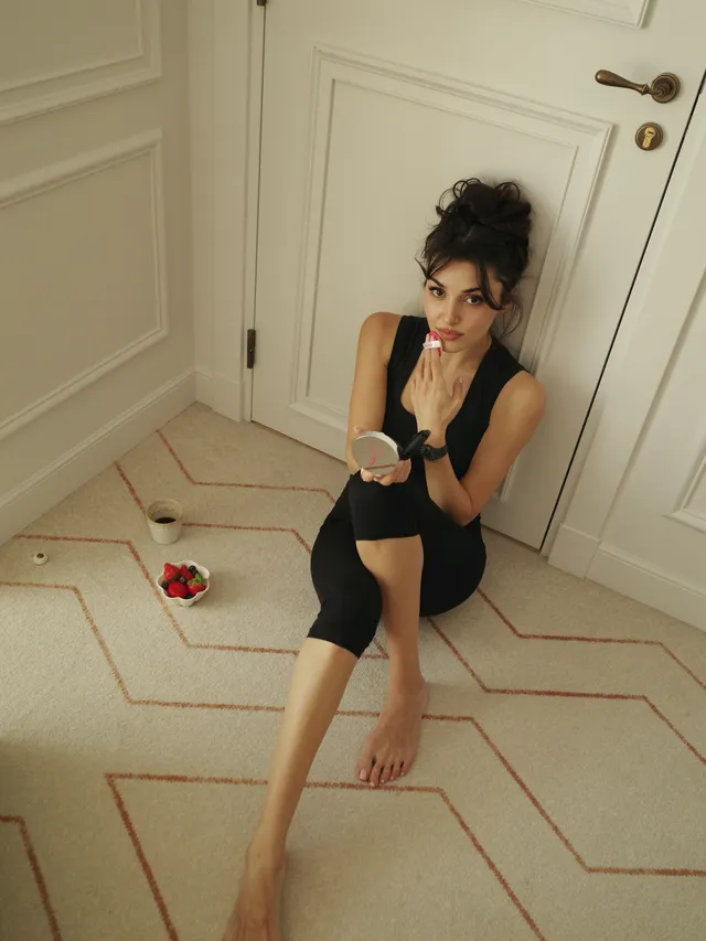 Hande Erçel sitting barefoot on a floor in a black dress.