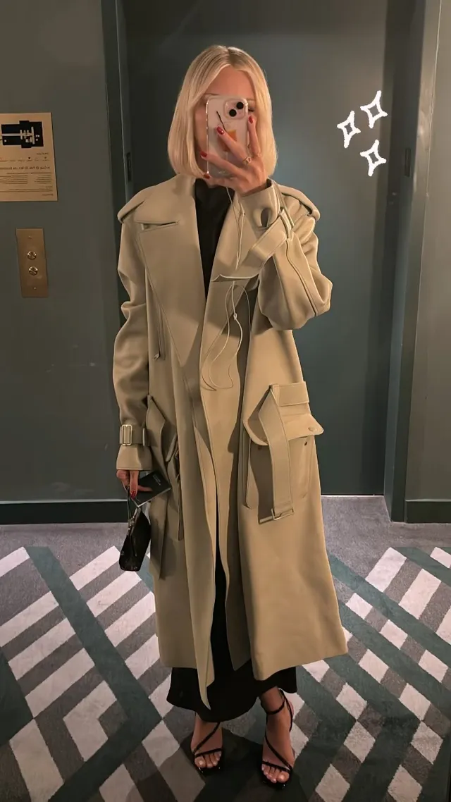 Grace VanderWaal taking a mirror photo in a tan coat and black heels.