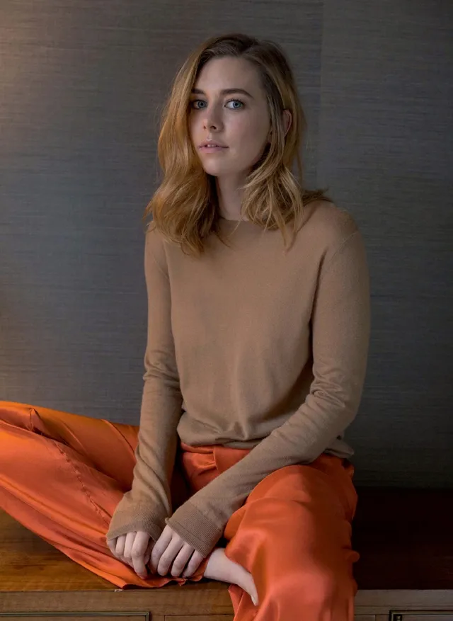 Vanessa Kirby a seated portrait in a pale top and orange trousers.
