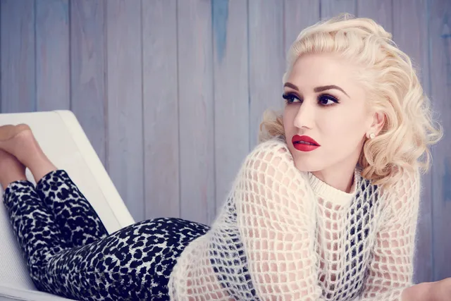 Gwen Stefani lying on a bed in a patterned outfit with bare feet raised.