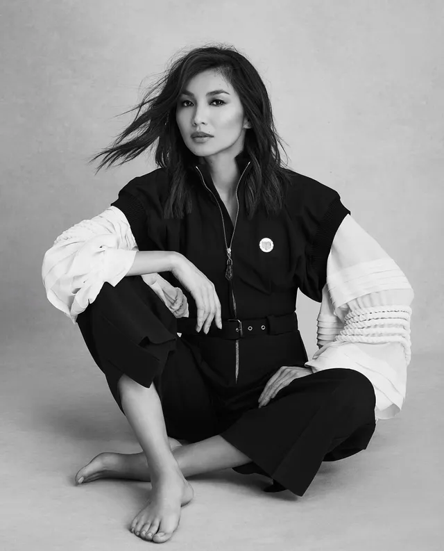 Gemma Chan sitting on the floor in a monochrome studio portrait.