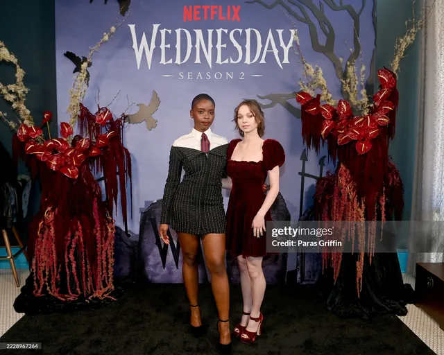 Emma Myers posing beside another woman at a premiere wearing red heels.