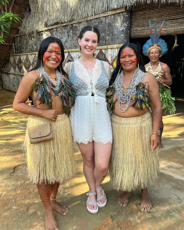 Lana Del Rey standing with other people in pale flat sandals.