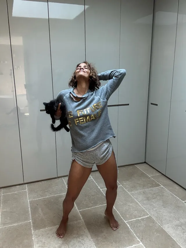 Halle Berry standing barefoot indoors in a gray top and shorts.