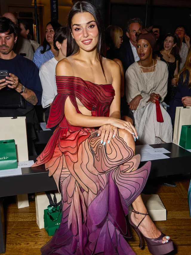 Hande Erçel sitting at an event in a flowing patterned gown and purple platform heels.