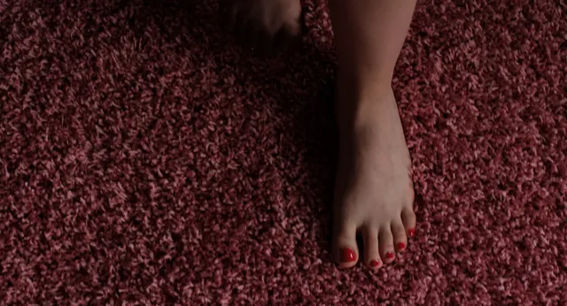 Cailee Spaeny showing red-painted toenails on a patterned carpet.