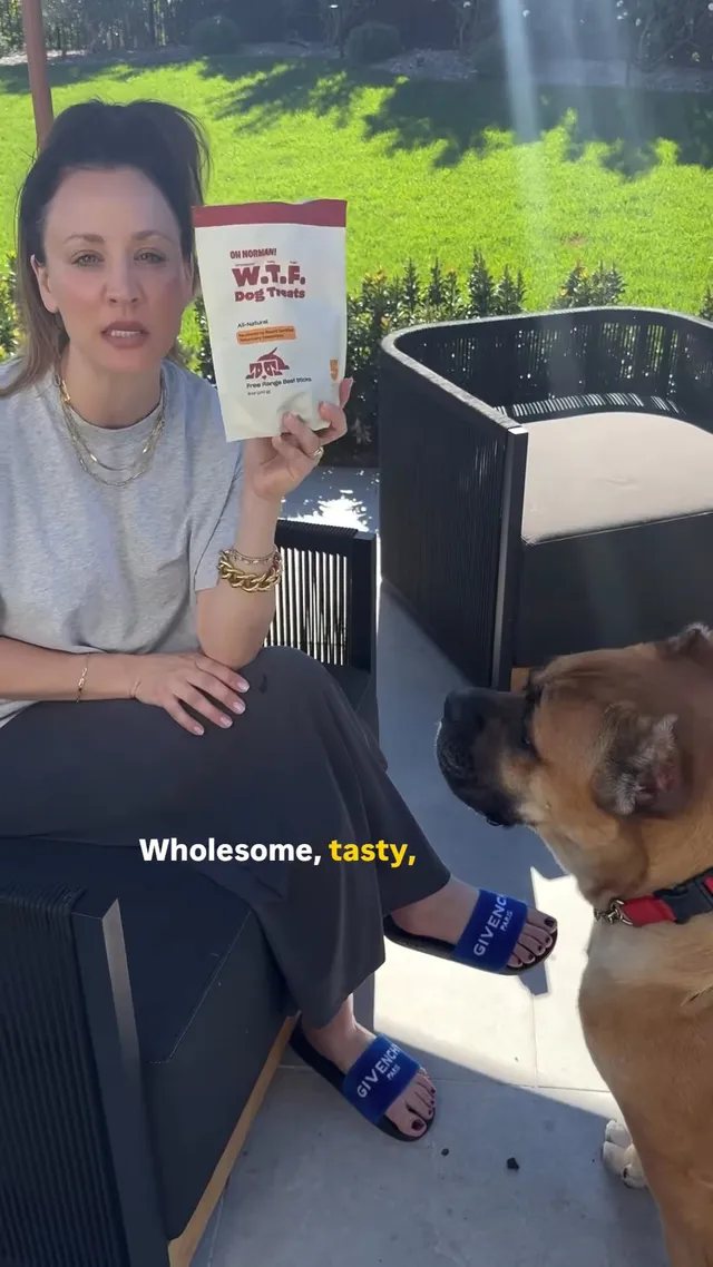 Kaley Cuoco standing beside a dog with a food bag while wearing blue slides.