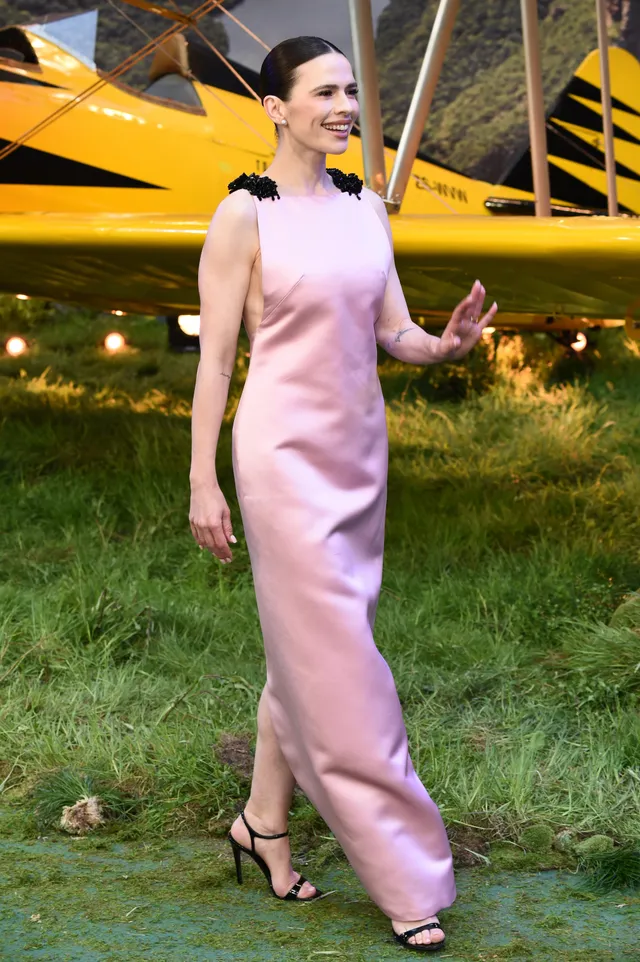 Hayley Atwell waving beside an aircraft in a pink gown.