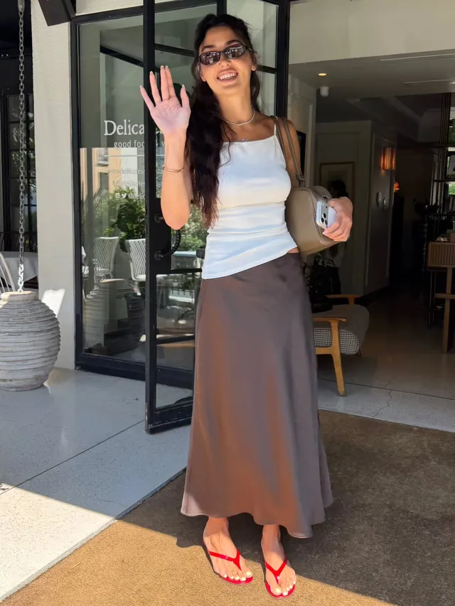 Hande Erçel posing outside a shop in a white top, long skirt and red flip-flops.