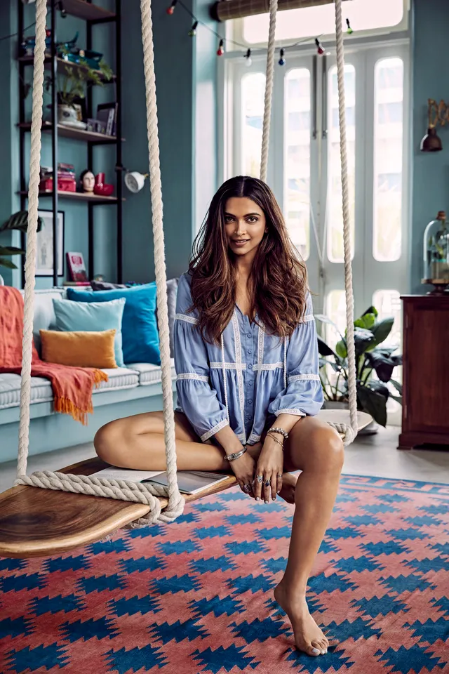 Deepika Padukone sitting barefoot on an indoor swing in a blue patterned outfit.