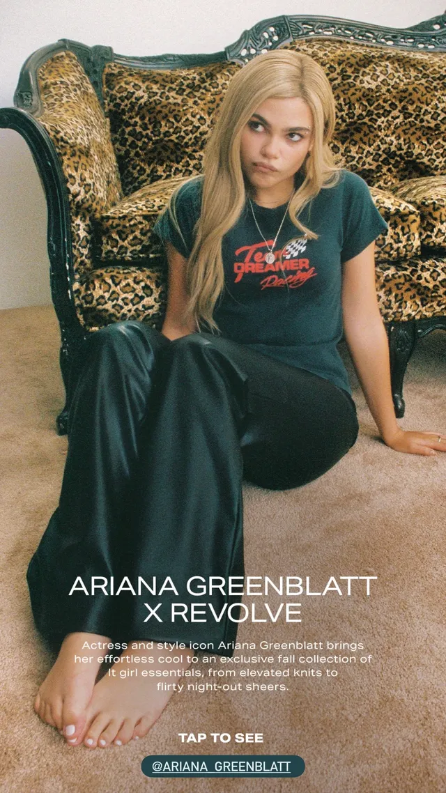 Ariana Greenblatt sitting barefoot on a patterned sofa in a dark outfit.