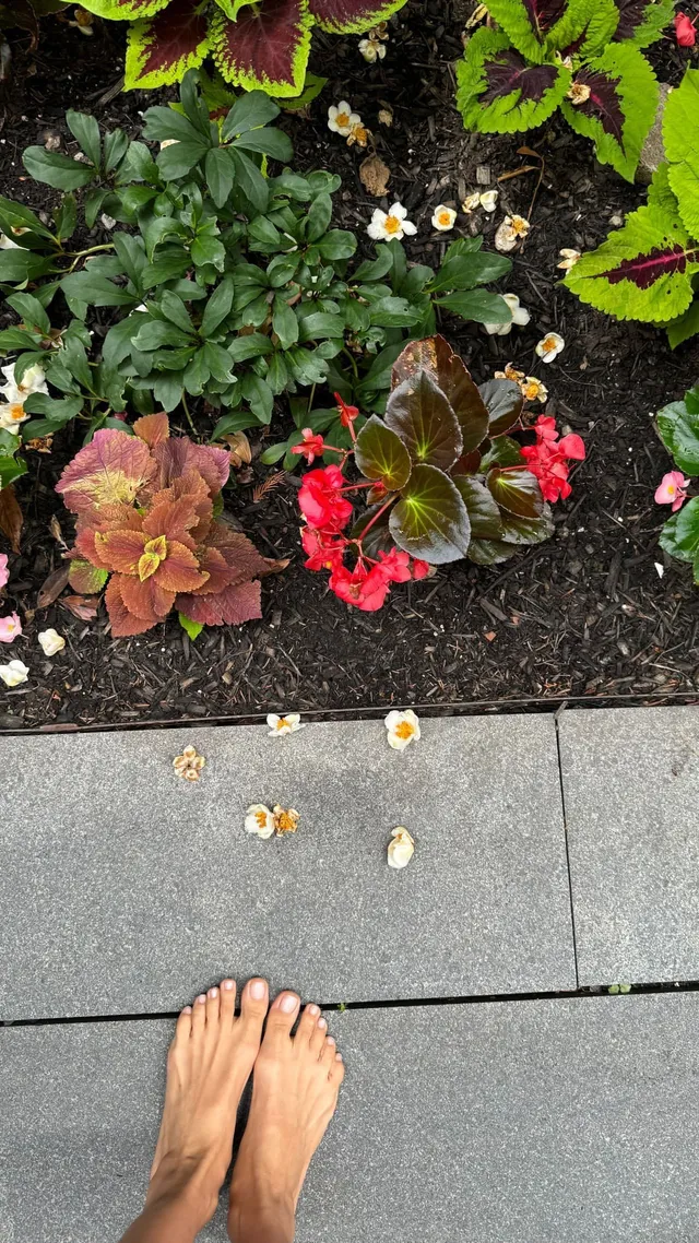 Irina Shayk bare feet beside a colourful flower bed.