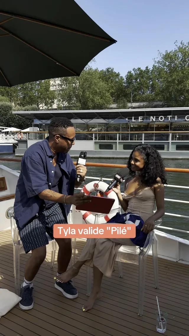 Tyla sitting in metallic heels beside an interviewer on an outdoor terrace.