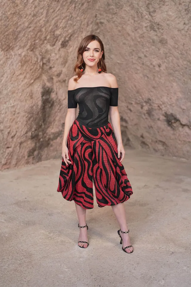 Kiernan Shipka posing in a black top, patterned skirt and black heels.