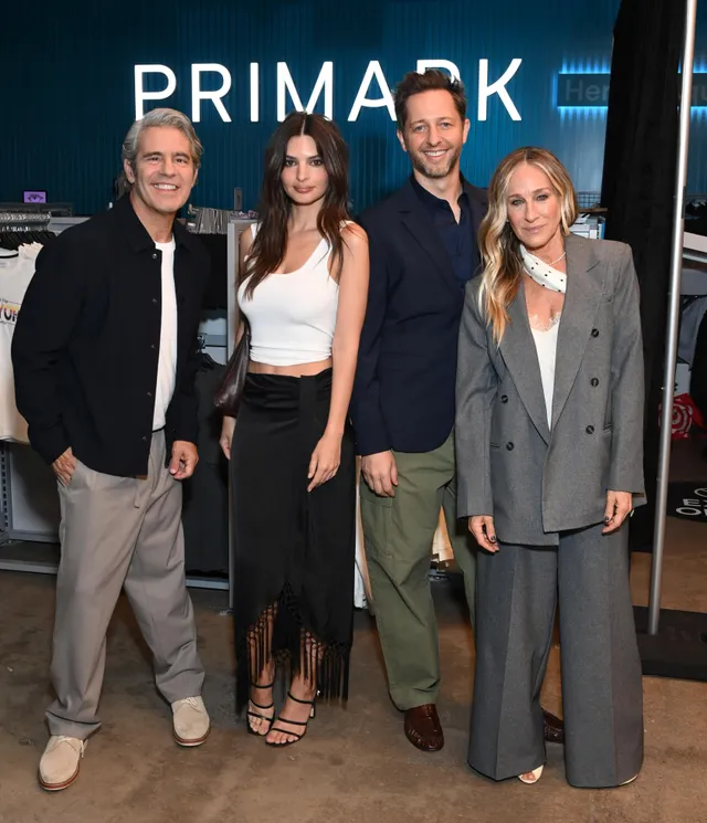 Emily Ratajkowski standing with a group wearing a white top and black heels.