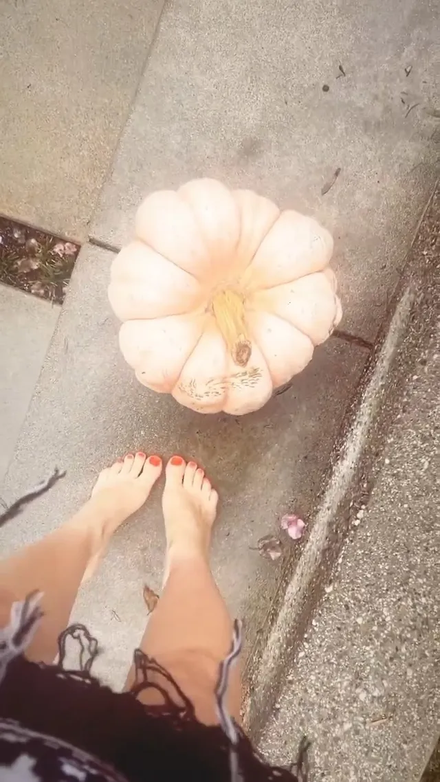 Avril Lavigne standing barefoot beside a pale pumpkin.