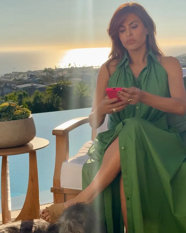Eva Mendes sitting in a green dress while looking at a phone.