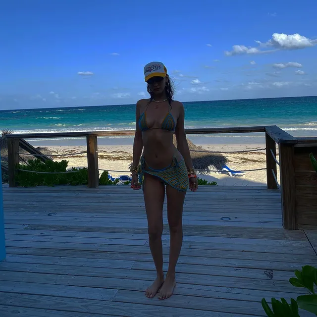 Bella Hadid walking barefoot across a deck beside the beach.
