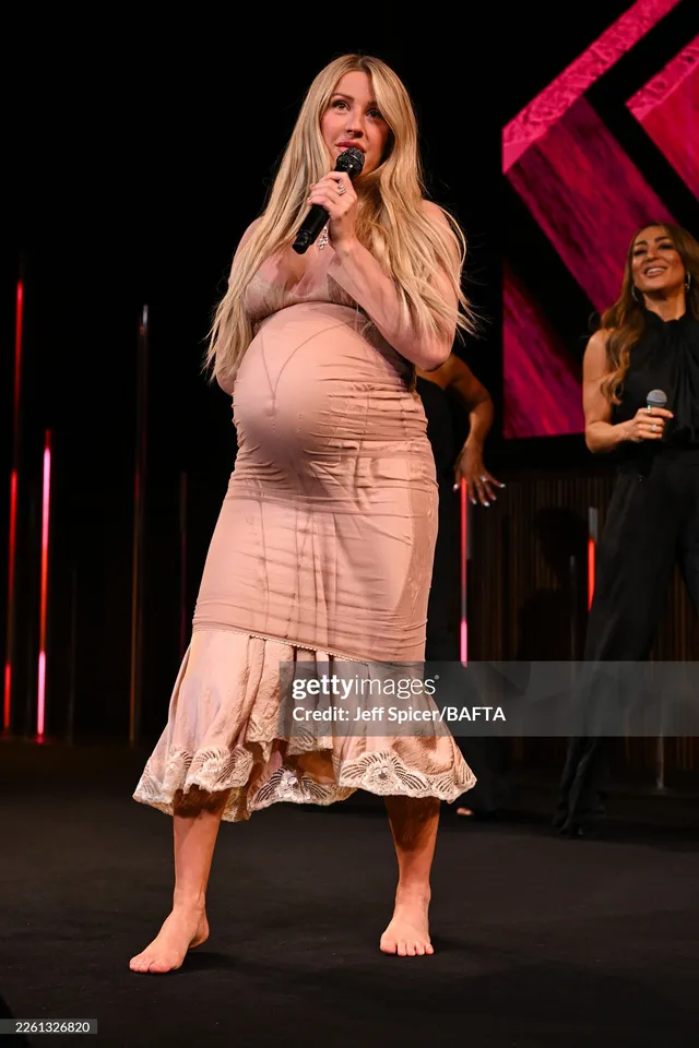 Ellie Goulding singing barefoot on stage in a pale dress.