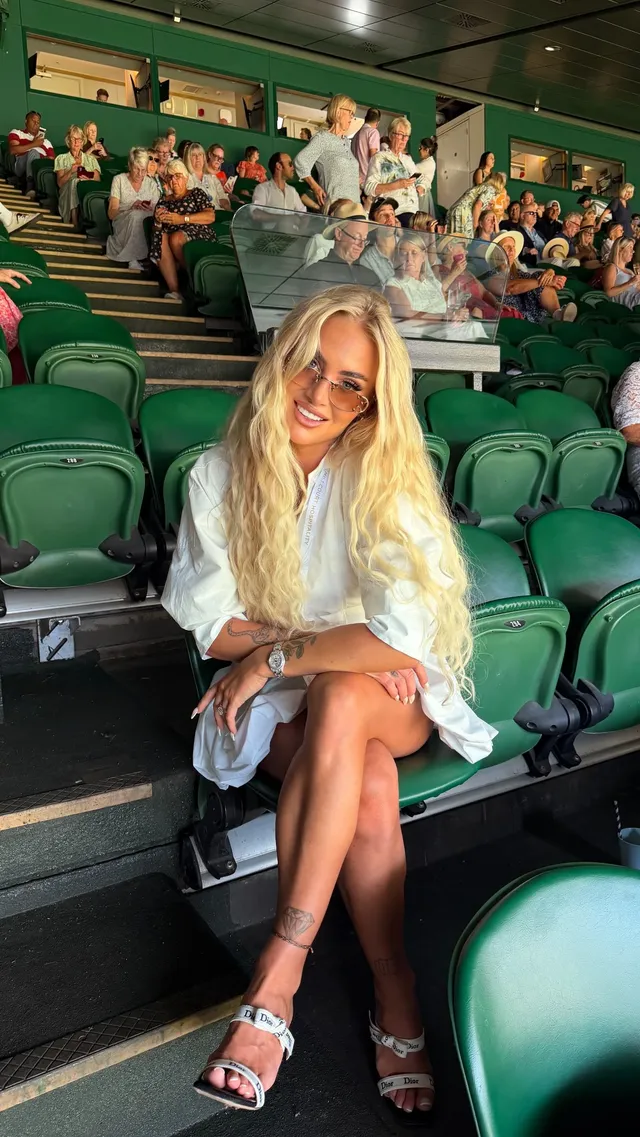 Alisha Lehmann sitting in spectator seating wearing metallic heeled sandals.