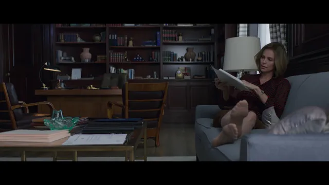 Charlize Theron a dimly lit screen scene relaxing on a sofa.