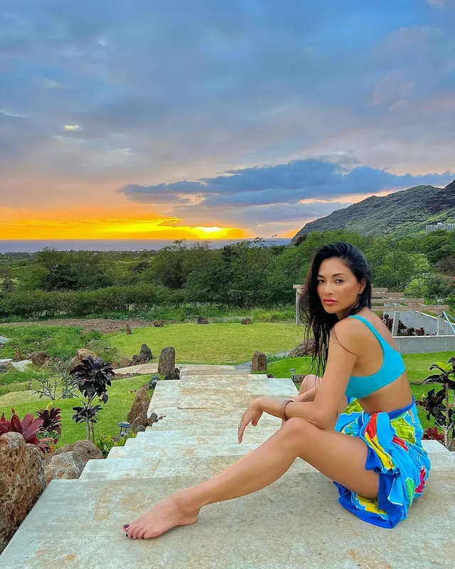 Nicole Scherzinger sitting barefoot outdoors in a colourful wrap.