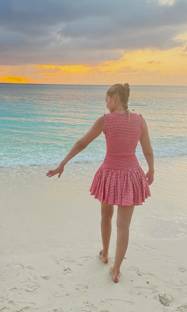Gigi Hadid walking barefoot on a beach in a pink dress.