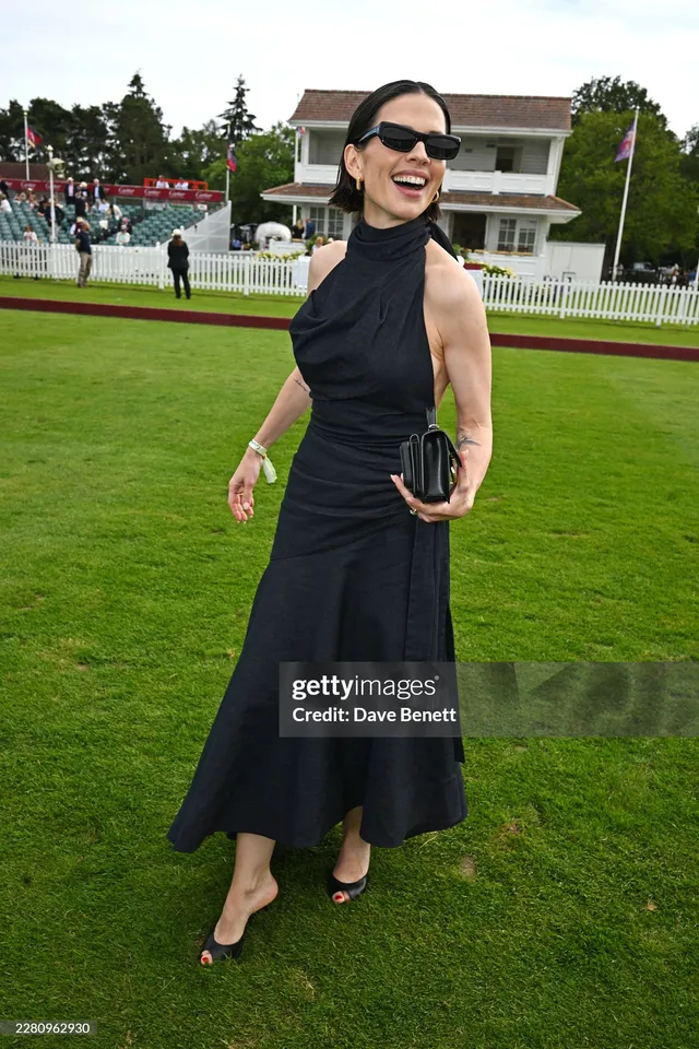 Hayley Atwell walking on a lawn in a black dress.