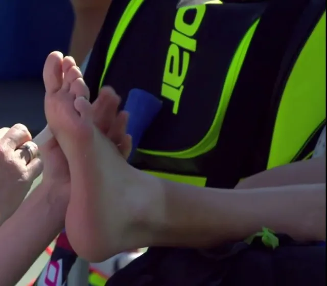 Eugenie Bouchard receiving treatment to her bare foot beside a tennis bag.