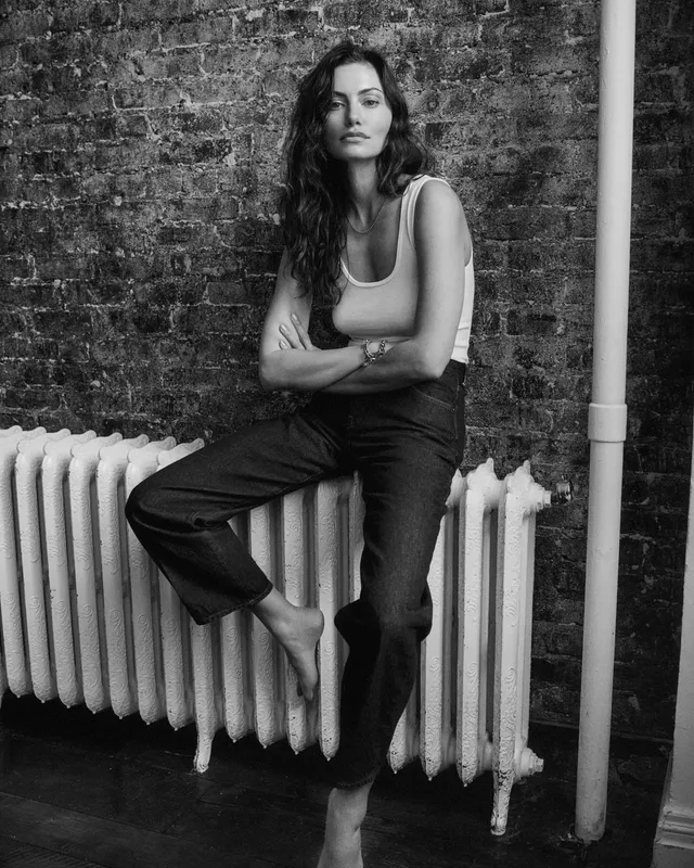 Phoebe Tonkin sitting on a radiator for a black-and-white portrait.