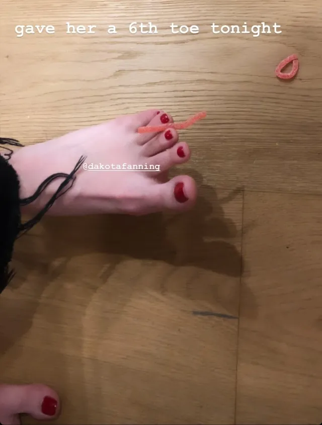 Dakota Fanning showing a red pedicure in an indoor photograph.