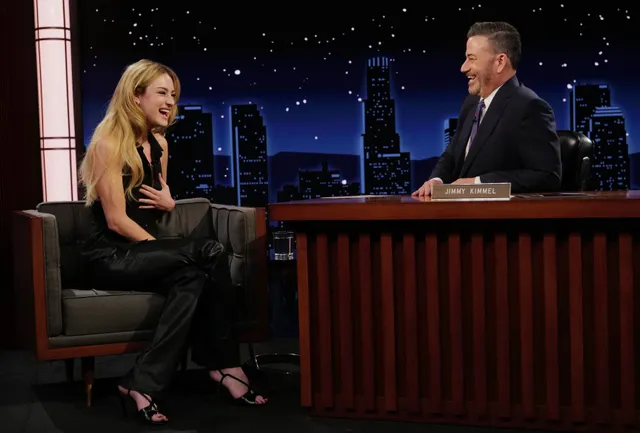 Grace Van Patten sitting opposite a talk show host in a black outfit and heels.