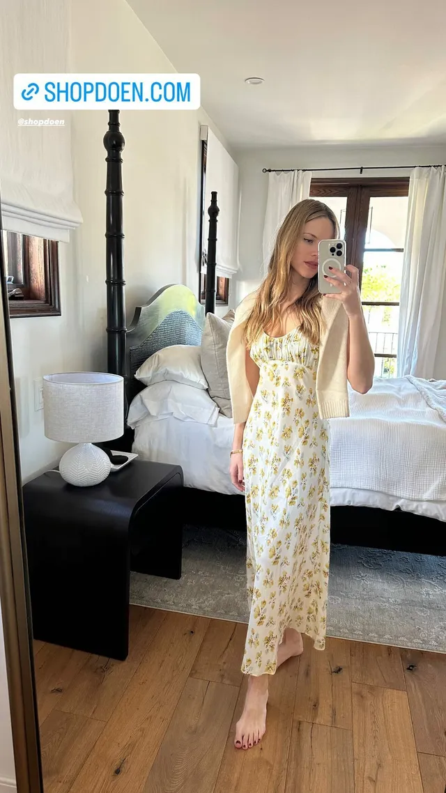 Halston Sage taking a mirror selfie barefoot in a long pale floral dress.