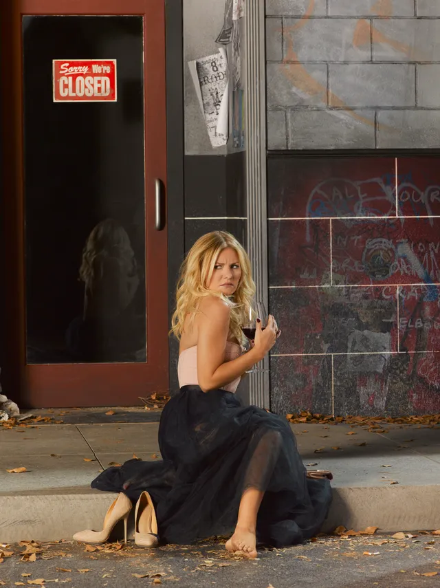Elisha Cuthbert sitting barefoot on steps while holding a glass.
