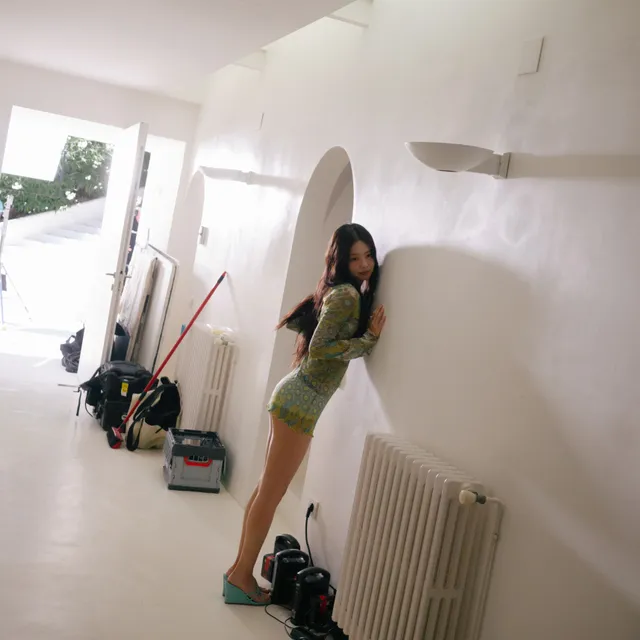 Jennie Kim standing barefoot in a short green outfit during a studio mirror photograph.