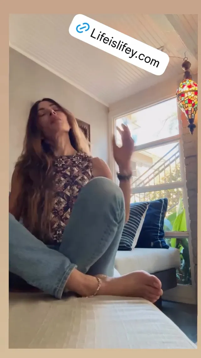 Sarah Shahi sitting on a sofa during a casual video.
