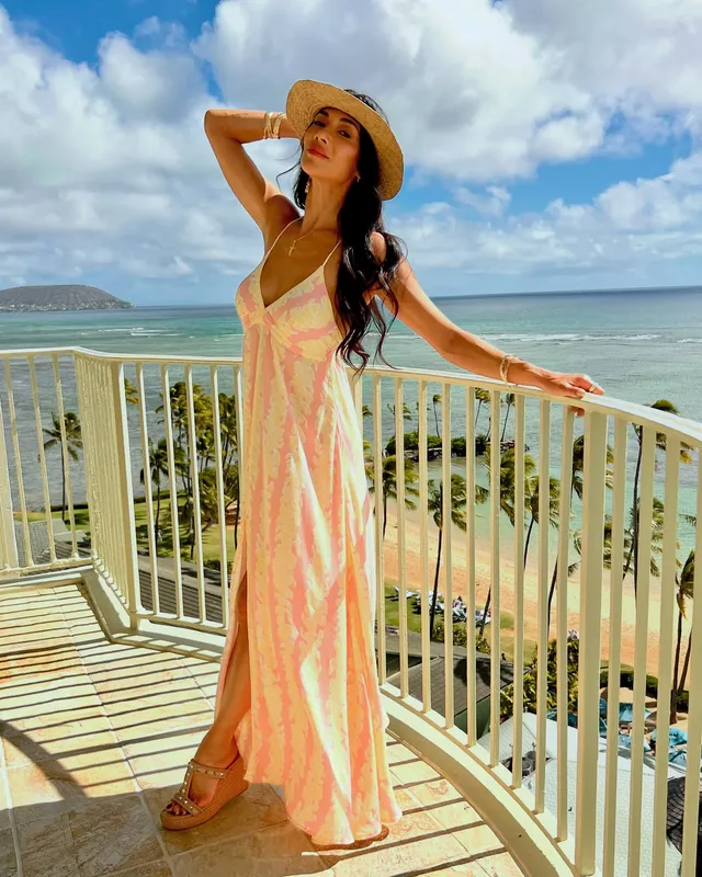 Nicole Scherzinger standing on a balcony in a long floral dress and platform heels.