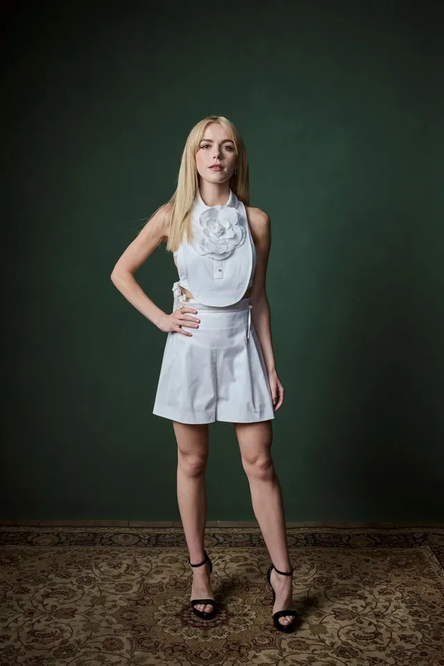 Kiernan Shipka posing in a pale outfit and black heeled sandals.