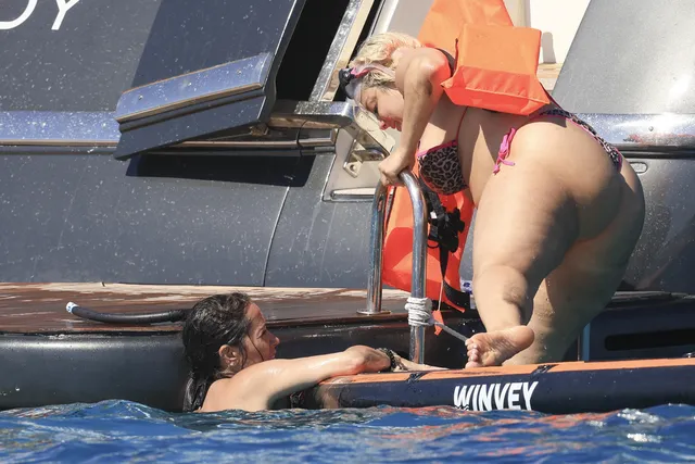 Bebe Rexha climbing from a paddleboard toward a boat.