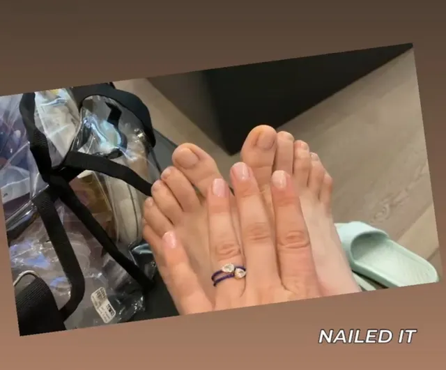 Kaley Cuoco showing her bare toes beside a hand with pale nail polish.