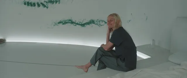Kate Bosworth sitting on a pale floor in a screen scene.