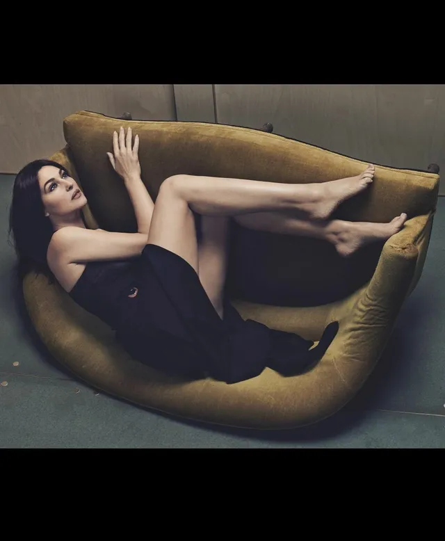 Monica Bellucci reclining on a brown sofa in a purple dress.