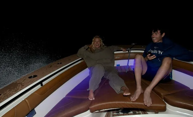 Iggy Azalea sitting barefoot on a boat beside another person at night.
