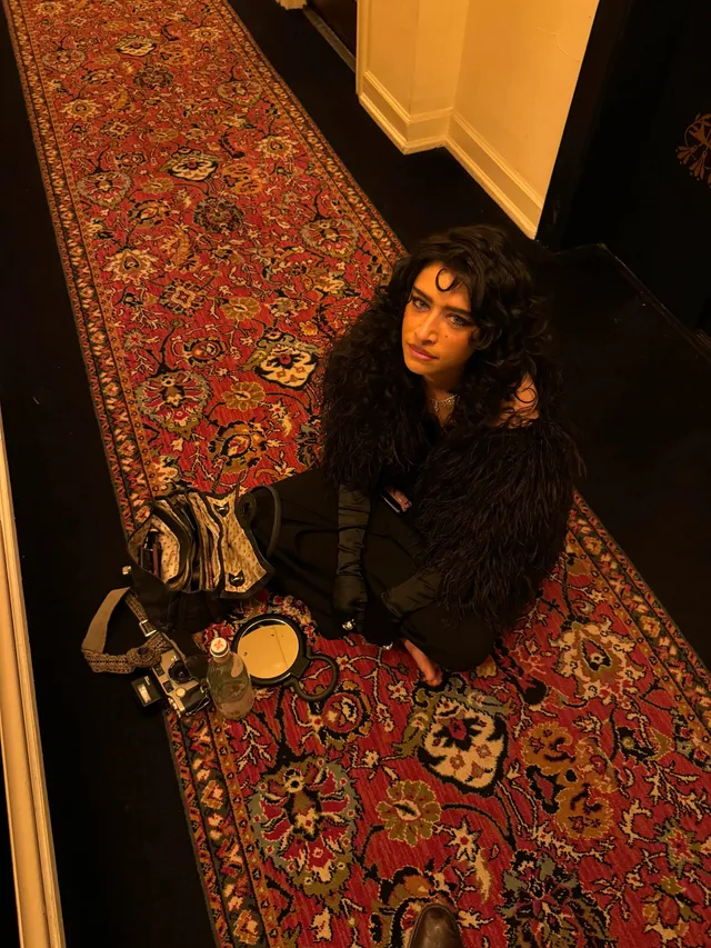 Odessa A'zion sitting on a rug in a dark outfit.