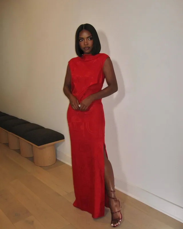 Ryan Destiny posing indoors in a long red dress and strappy heels.