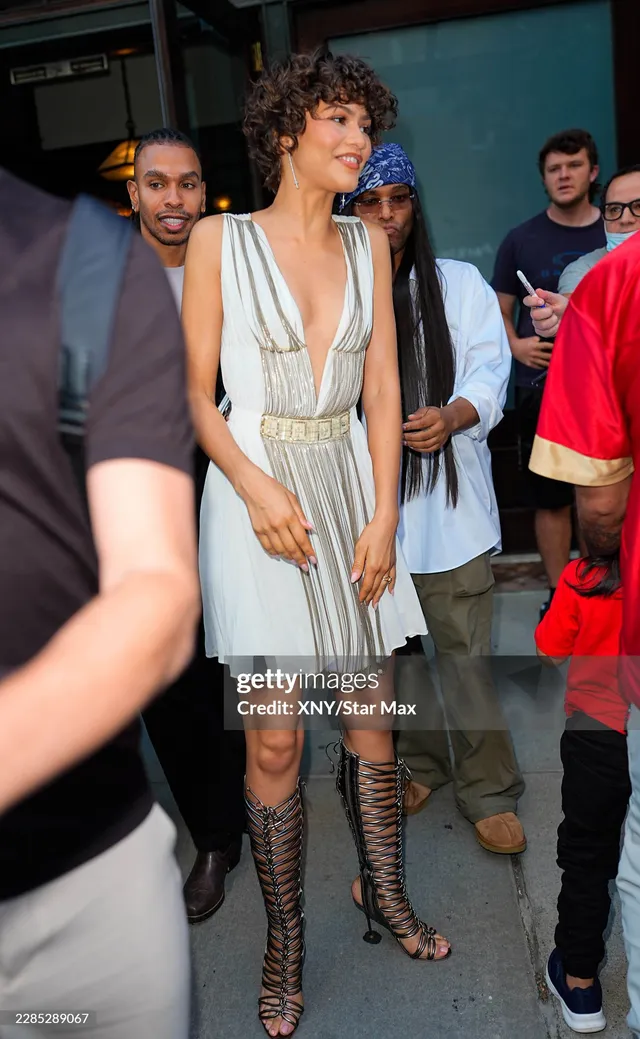 Zendaya walking through a crowd in a light dress and tall lace up heels.