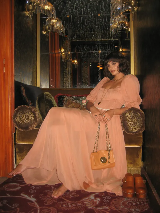 Taylor Hill sitting barefoot in an ornate room wearing a long pale dress.