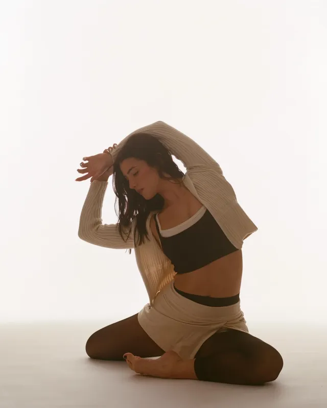 Charli D’Amelio posing barefoot in a studio wearing a cream outfit.
