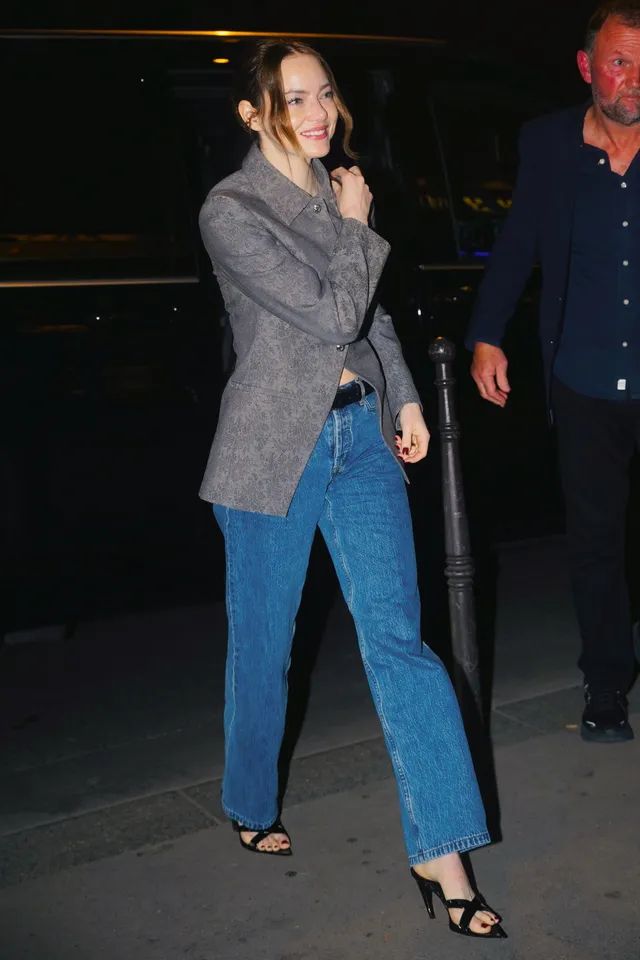 Emma Stone walking in blue jeans, a gray blazer and open-toe heels.